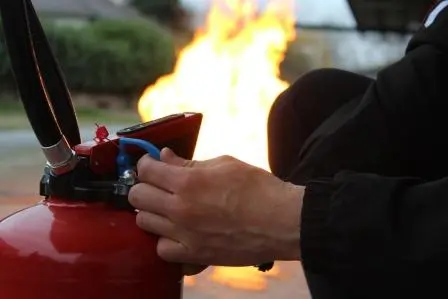 Main utilisant un extincteur près d'un feu.